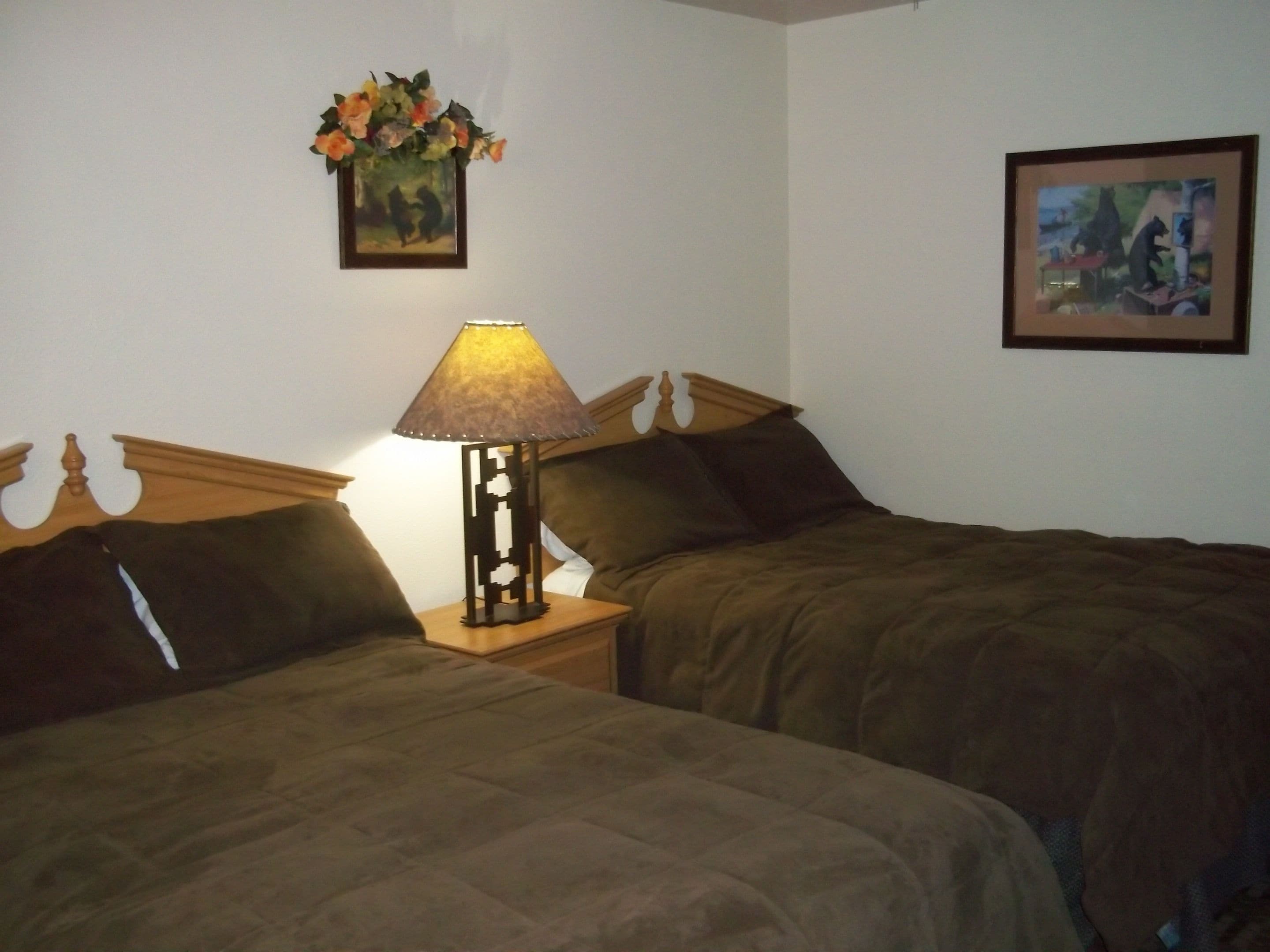 A hotel room with two beds, a nightstand with a lamp, and two framed pictures on the walls.