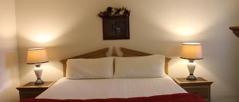 A neatly made bed with a wooden headboard, two bedside lamps, and a wall-mounted picture frame.