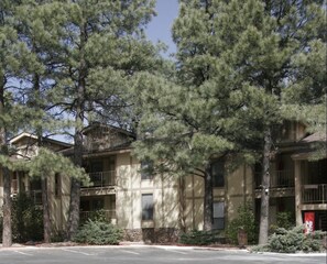 A two-story building with balconies, surrounded by pine trees. - Village Lodge Condos (Ruidoso)