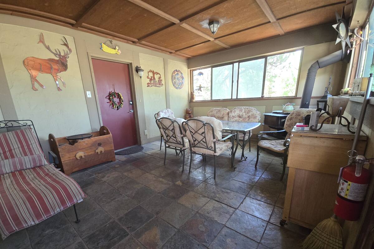 Een rustiek houten interieur met houten balkenplafond, stenen vloer en een eethoek met bloemrijk gestoffeerde stoelen.