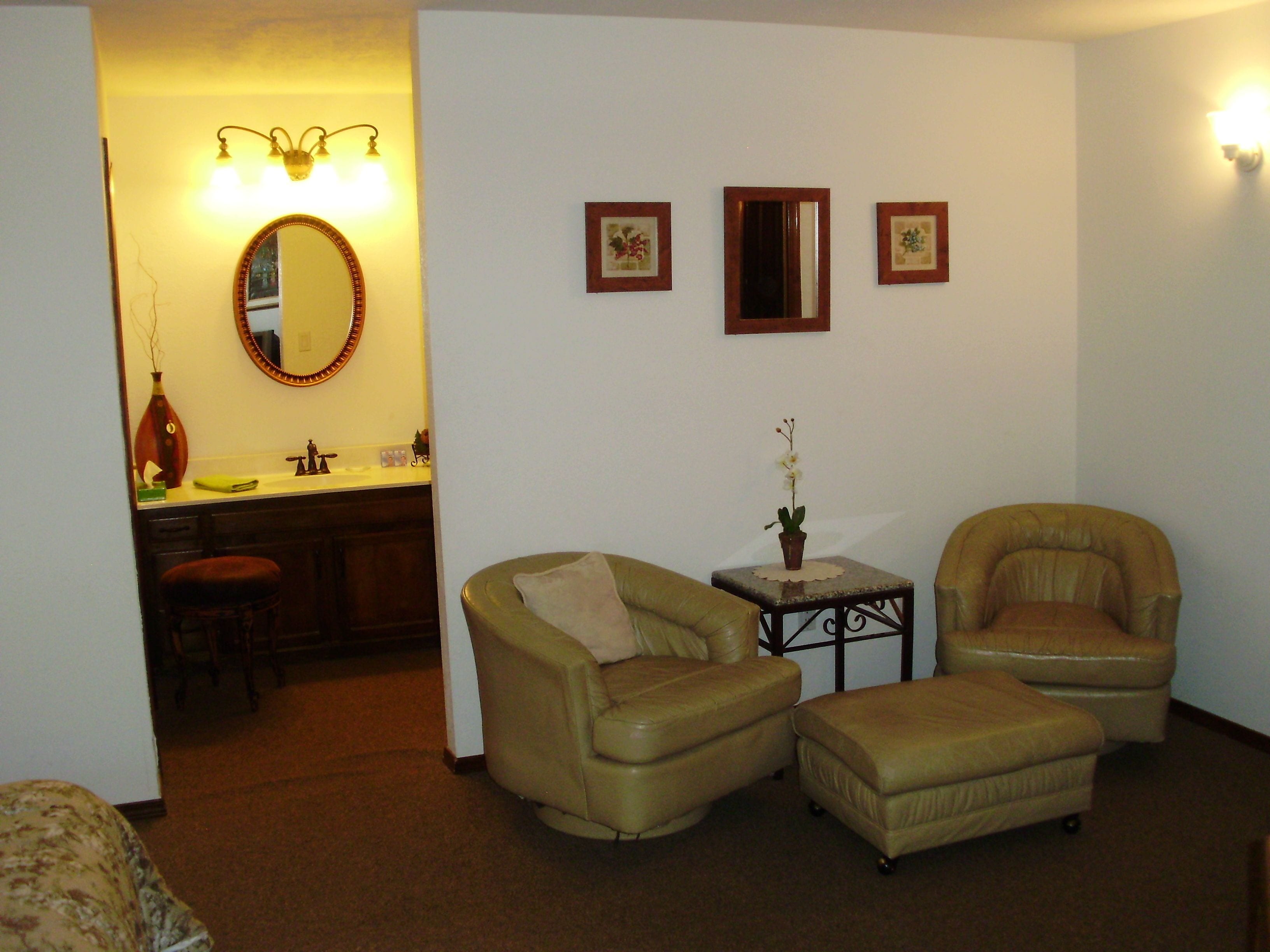 A living room with two leather armchairs, a small table with a vase, a mirror, and a sofa.