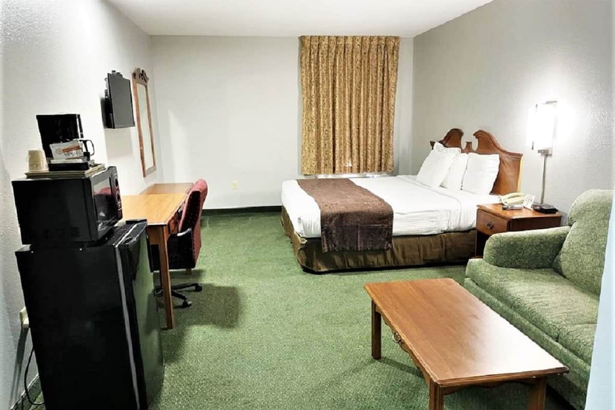 Una habitación de hotel con una cama, un escritorio con computadora, una silla, una mesita y un sofá.