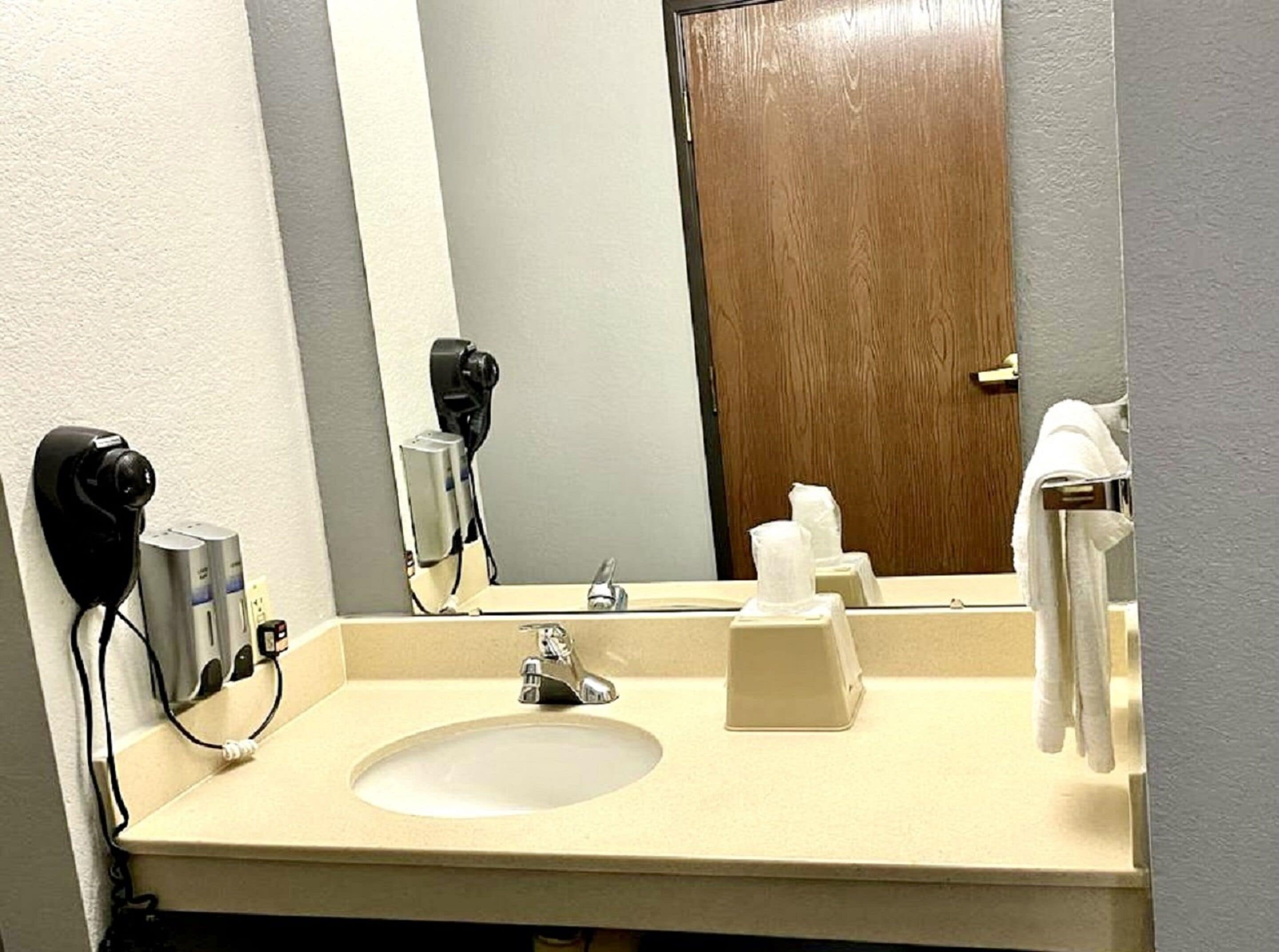 Un baño de hotel con lavamanos, espejo, dispensador de toallas y secador de pelo.