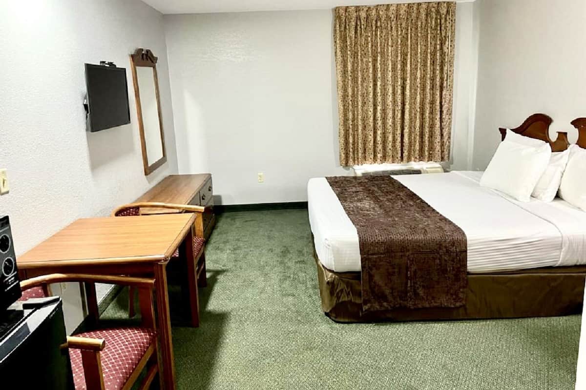 Habitación de hotel con cama, escritorio, silla, televisión y ventana con cortinas.