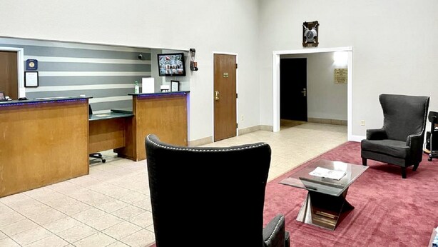 A reception area with a wooden desk, a black leather chair, and a red carpet. - Star City Inn & Suites (Star City)