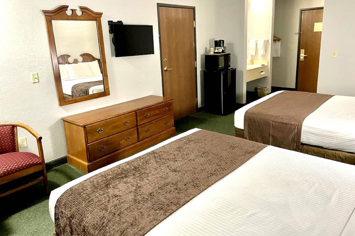 Una habitación de hotel con dos camas, un aparador, un espejo, un televisor y una cafetera.