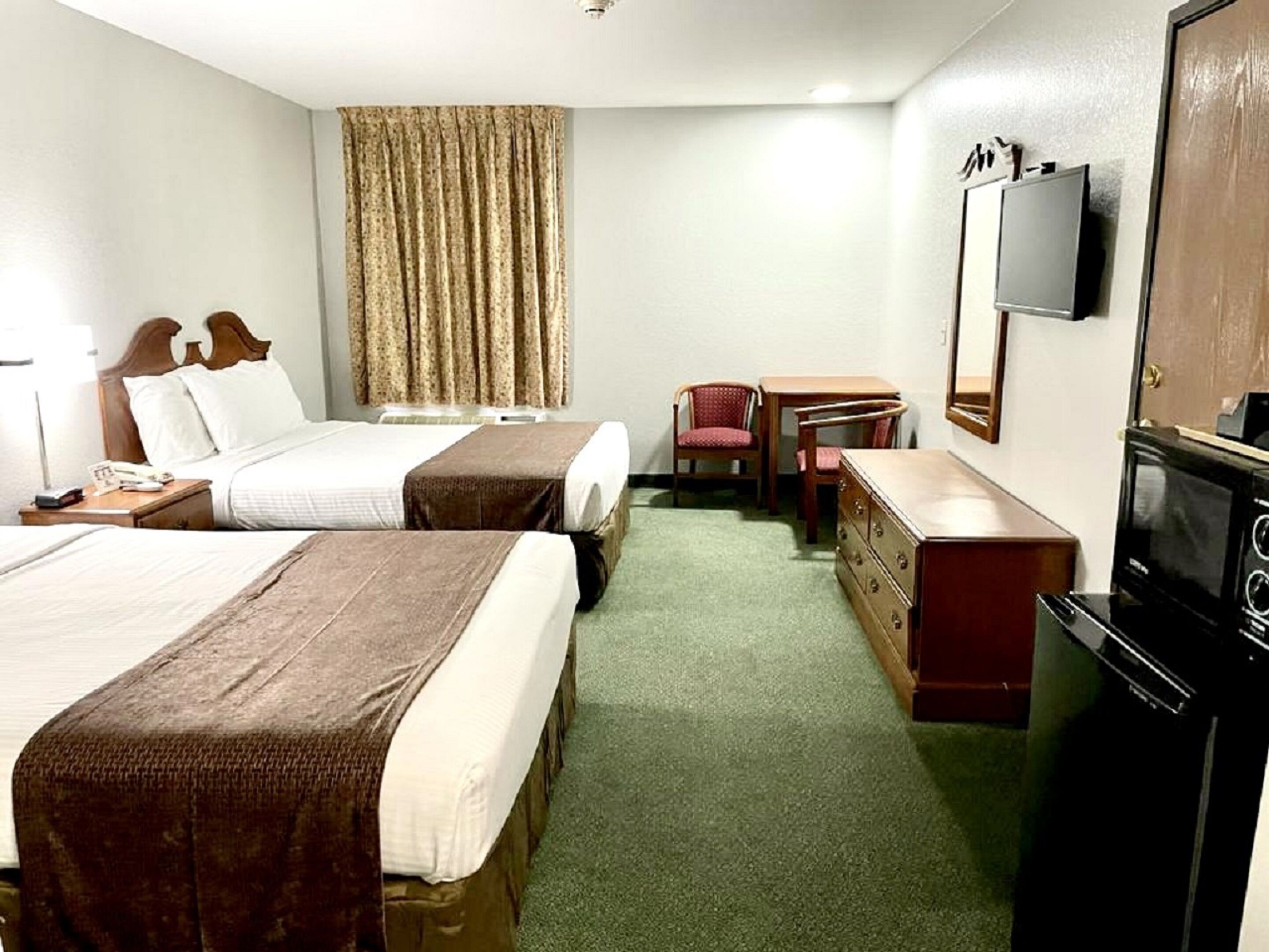 Habitación de hotel con dos camas, un escritorio, una silla, un aparador, televisión y microondas.