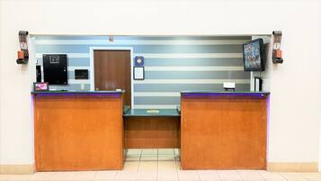A reception area with two wooden reception desks, a digital screen, a door, and a wall-mounted television.