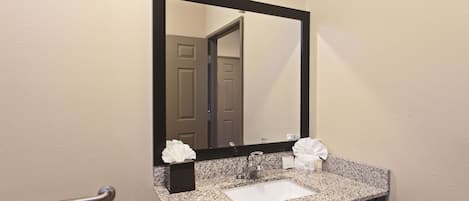 A bathroom with a granite countertop sink, a mirror, and a towel dispenser.