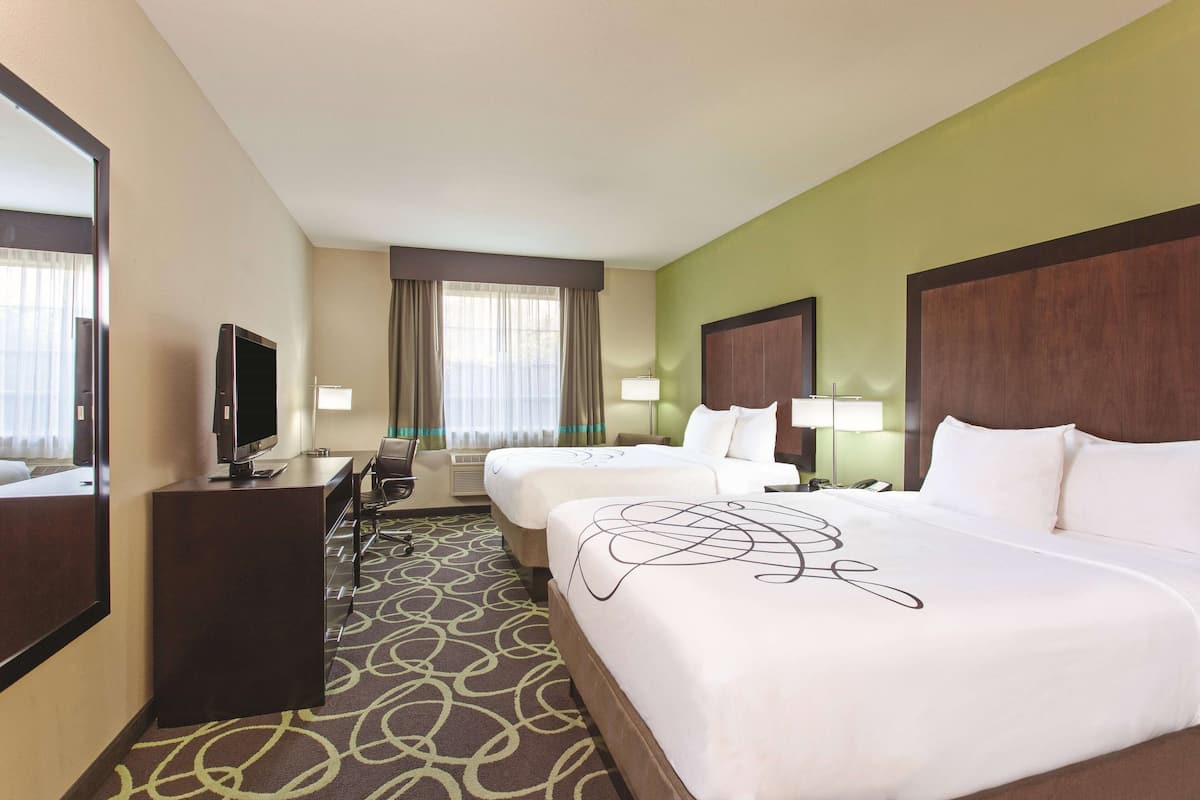 A hotel room with two beds, a desk with a television, a chair, and a large mirror.