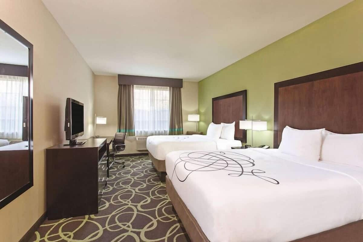 A hotel room with two beds, a desk, a television, and a large mirror.