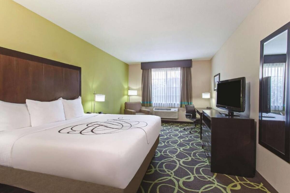A hotel room with a bed, a desk, a television, and a window with curtains.
