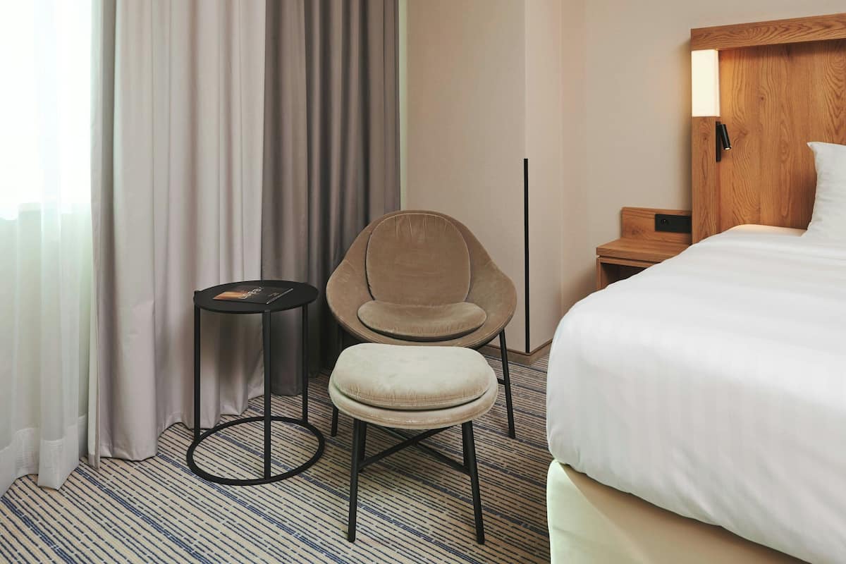Una camera d'albergo con un letto, una sedia, un tavolino e un comodino.