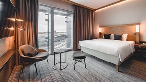 Une chambre d’hôtel avec un grand lit, un bureau, une chaise, un petit tabouret et un téléviseur.