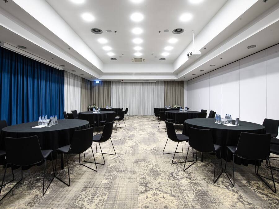 Una sala conferenze con tavoli rotondi, sedie nere e una moquette fantasia.