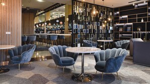 Un intérieur moderne avec des tables rondes et des fauteuils en velours, un coin bar à l’arrière-plan et un mur décoratif orné de tableaux encadrés.