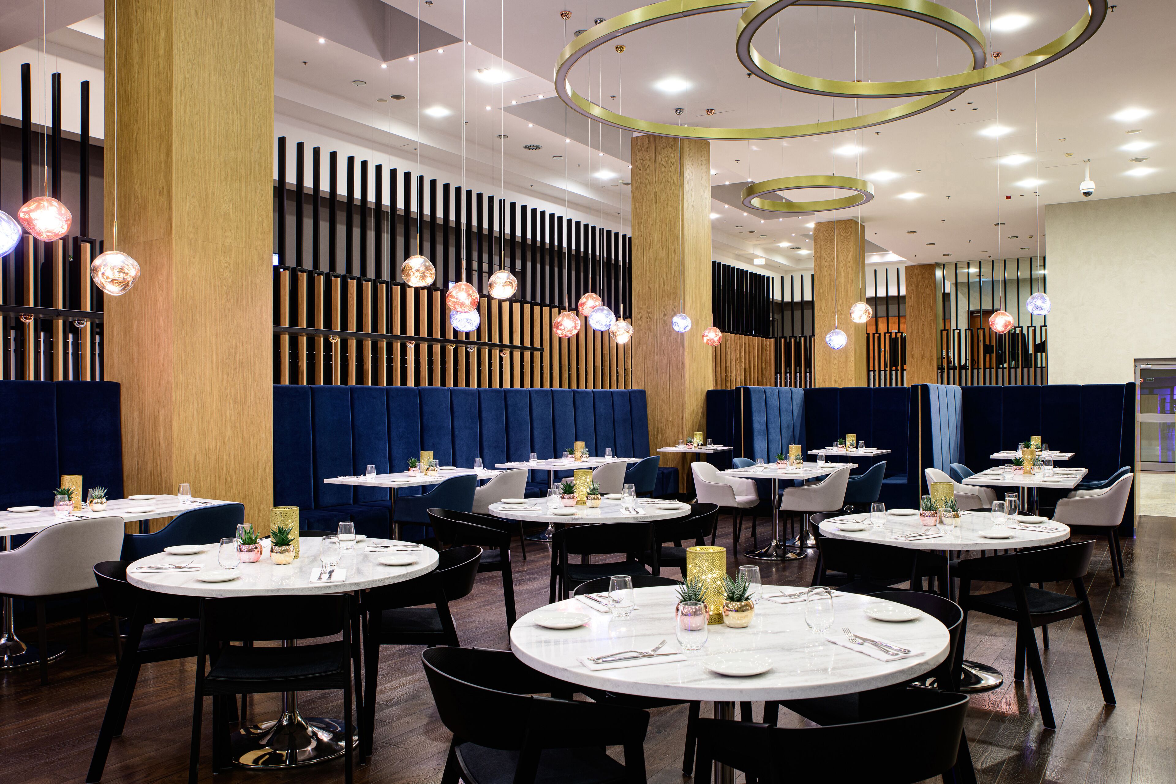 A modern restaurant interior with round tables, black chairs, and decorative hanging lights.