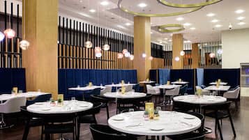 A modern restaurant interior with round tables, black chairs, and decorative hanging lights.