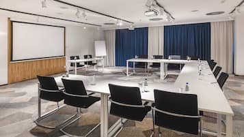 A conference room with a long table, black chairs, a whiteboard, and a projector screen.