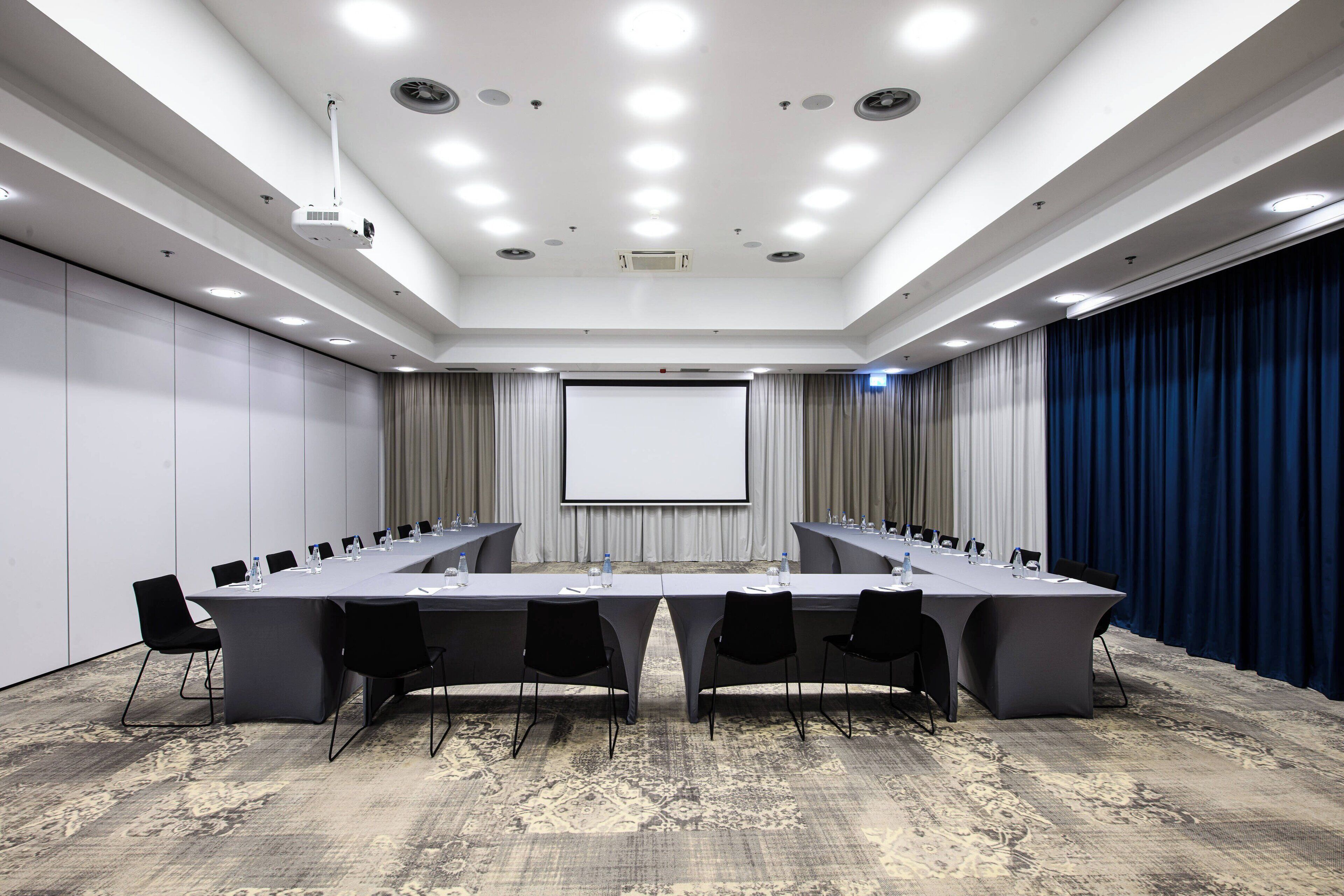 A conference room with a long table, chairs, a projector, and a screen.