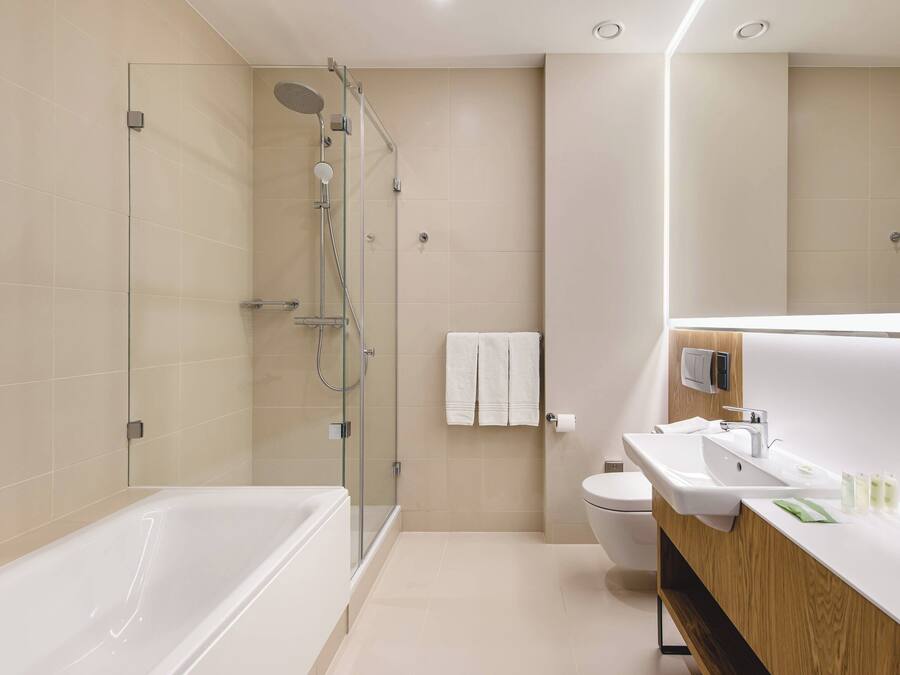 A modern bathroom with a glass-enclosed shower, a bathtub, a sink with a wooden vanity, and a toilet.