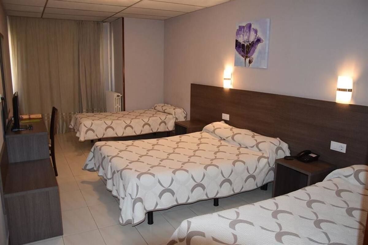 Hotellihuone, jossa on kolme sänkyä, työpöytä ja tuoli.