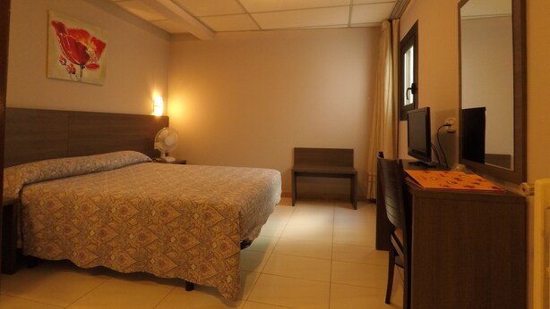 Une chambre d’hôtel comprenant un lit, un bureau avec un ordinateur, une chaise, un téléviseur fixé au mur et un luminaire au plafond.