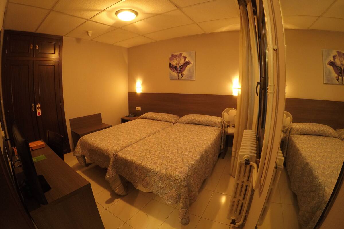 Hotellihuone, jossa on suuri sänky, yöpöydät, työpöytä ja patteri.