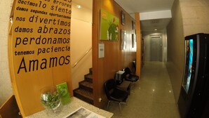 Un pasillo con pared de madera decorada con texto motivacional, un cuenco de vidrio con plantas y una zona de estar con sillas y una mesa.