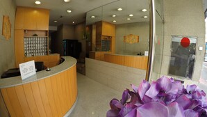 Un área de recepción con mostrador de madera curvada, una mesa de registro y una partición de vidrio.