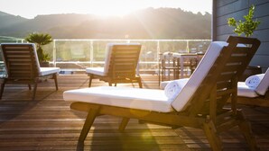 A wooden deck with lounge chairs and a table, overlooking a scenic view with hills in the background.