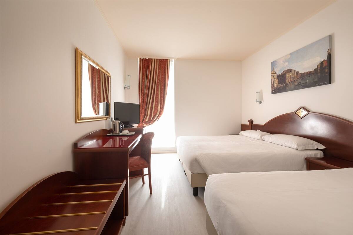 A hotel room with two beds, a desk with a chair, a television, and a painting on the wall.