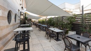 An outdoor patio with tables and chairs, a white canopy, and a building with arches in the background. - Noventa Hotel (Noventa di Piave)