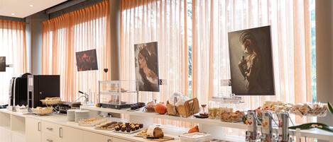 A buffet setup with various food items and beverages, a coffee machine, and a security camera on the ceiling.