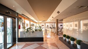 A modern hotel lobby with a reception desk, seating area, and a large window. - Noventa Hotel (Noventa di Piave)