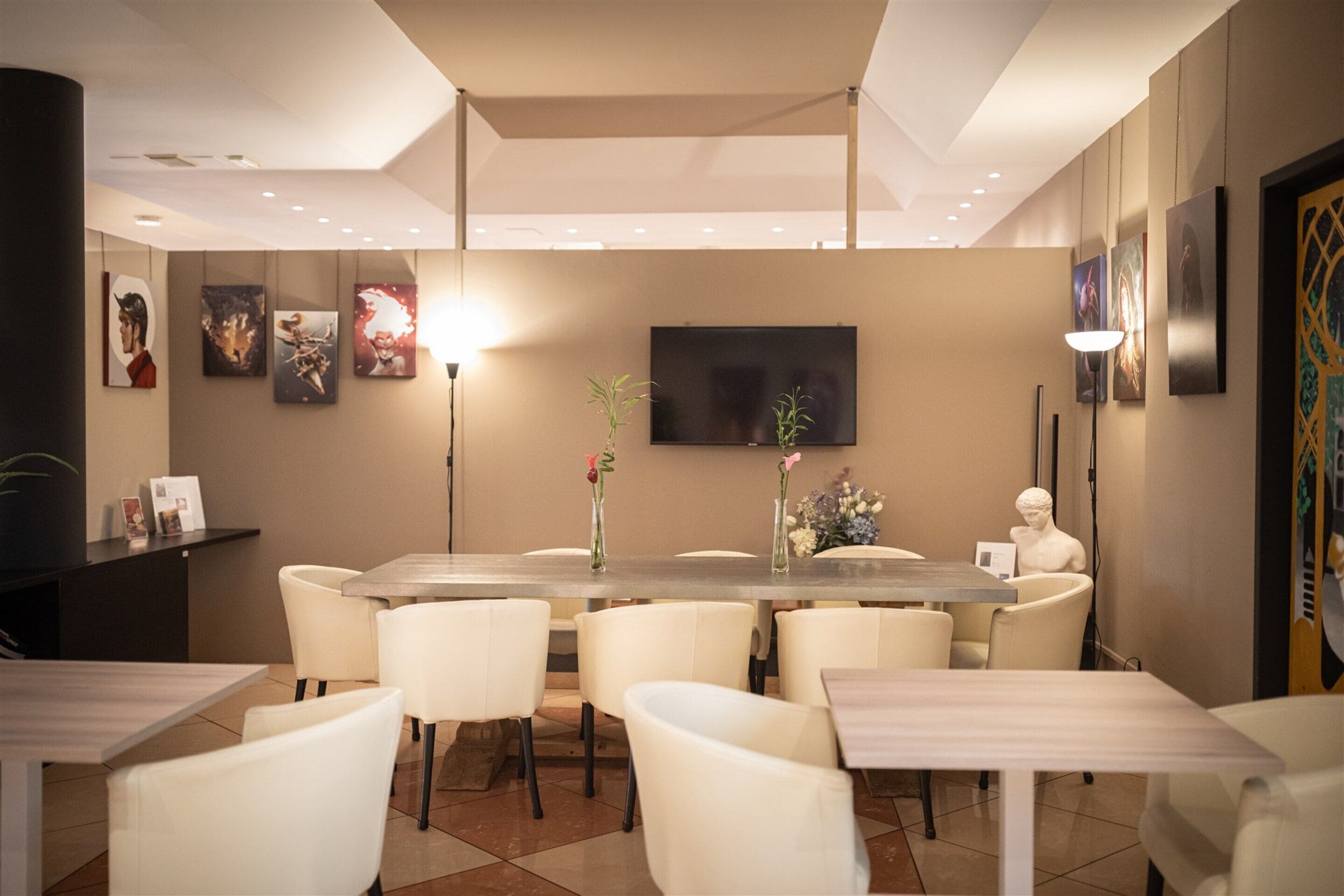 A modern dining area with a long table, white chairs, and a flat-screen TV mounted on the wall.