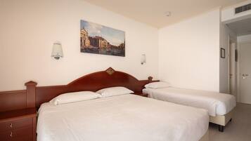 A hotel room with two beds, a wooden headboard, a painting of a cityscape, and a door to the right.