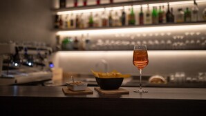 A bar area with a glass of wine, a bowl of snacks, and a bottle of liquor on shelves. - Noventa Hotel (Noventa di Piave)