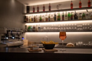 Una zona de bar con una copa de vino, un bol de aperitivos y una botella de licor en estantes.