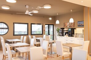 A modern cafe with multiple tables and chairs, ceiling fans, and a coffee station.