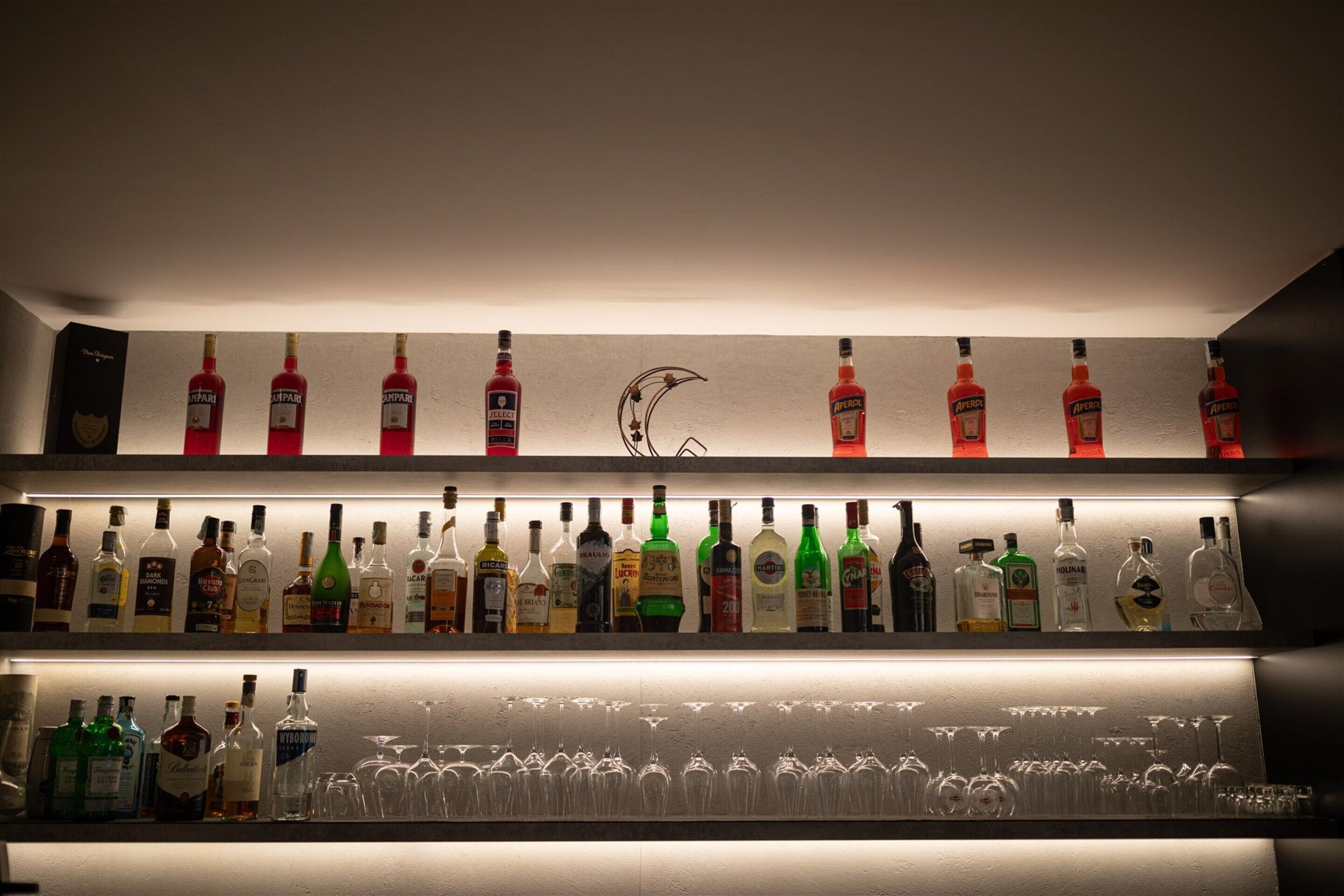 A bar area with shelves of liquor bottles and wine glasses.