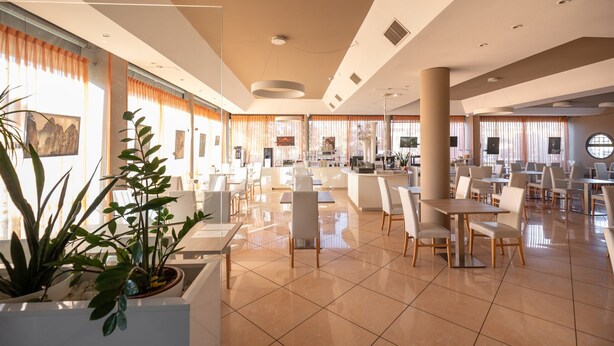 A spacious hotel lobby with multiple seating areas, large windows, and potted plants. - Noventa Hotel (Noventa di Piave)