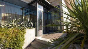 A modern building with a glass entrance, a concrete planter with greenery, and a brick pathway. - Noventa Hotel (Noventa di Piave)