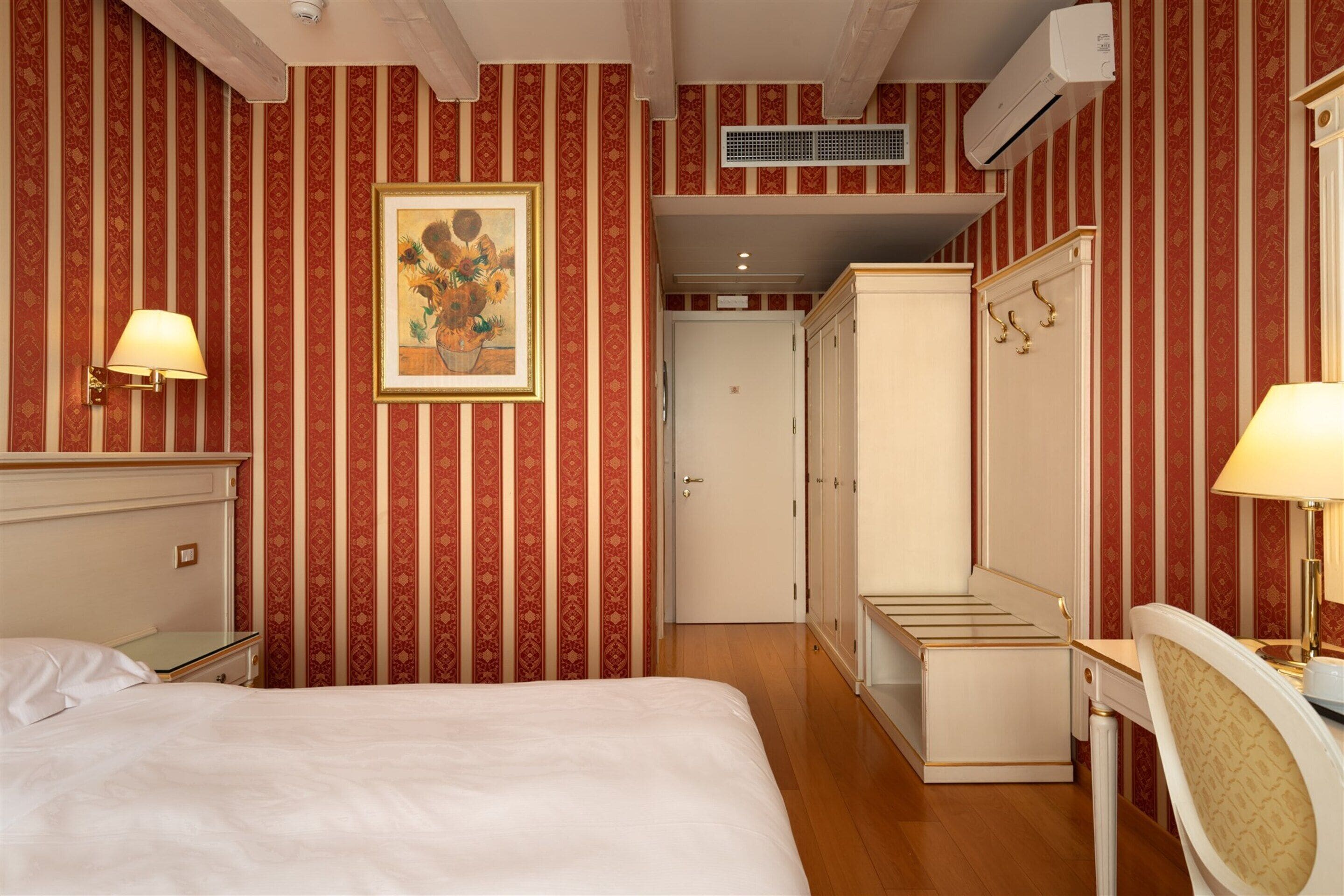 Una habitación de hotel con cama, escritorio, armario y un cuadro en la pared.