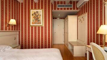 Una habitación de hotel con cama, escritorio, armario y un cuadro en la pared.