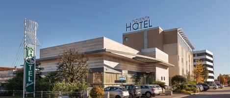 Hotel Noventa, con un diseño moderno, presenta un letrero llamativo, un estacionamiento con varios autos y un cielo despejado.