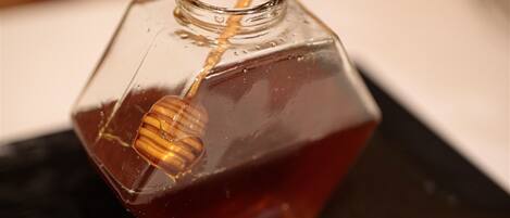 A honey jar with a wooden lid and a honey dipper on a black surface.
