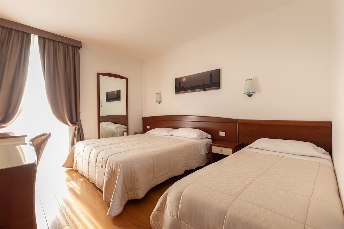 A hotel room with two beds, wooden headboards, a desk, and a chair.