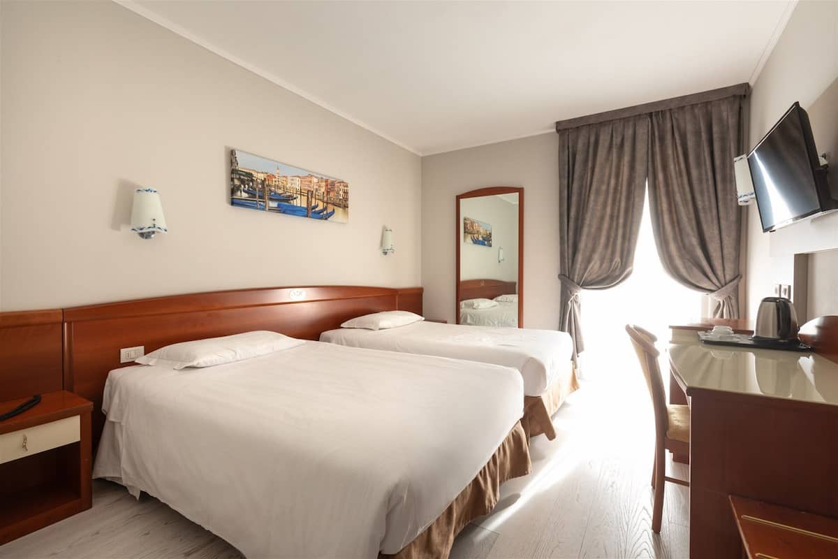 A hotel room with two beds, a desk, a chair, a television, and a window with curtains.