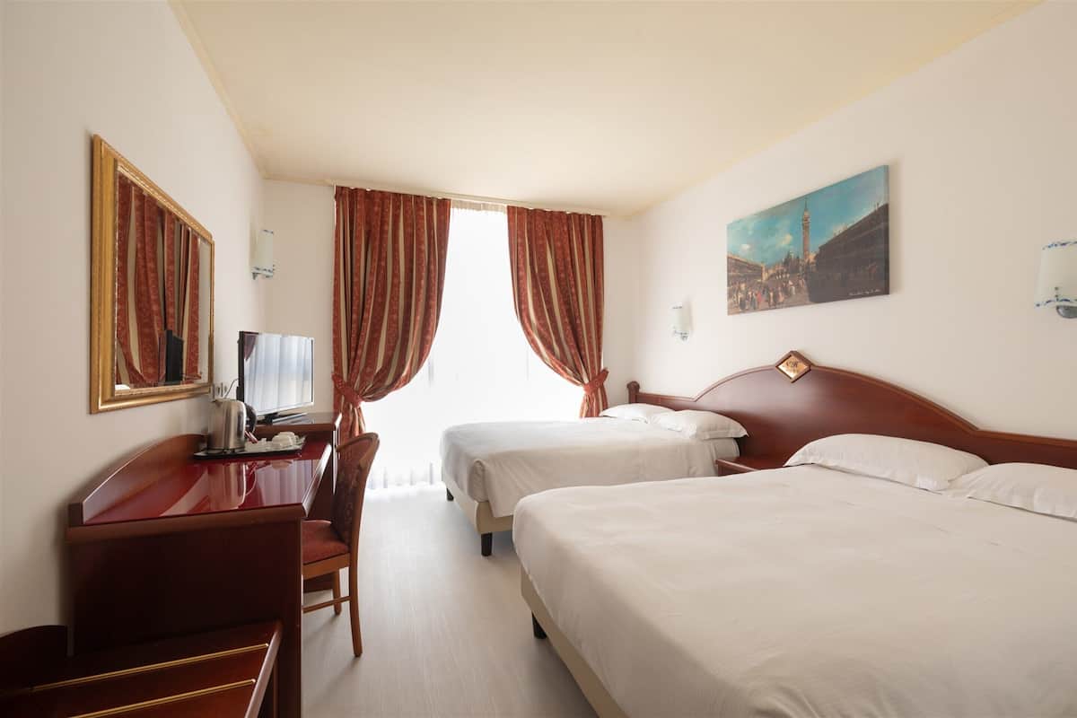 A hotel room with two beds, a desk, a chair, and a painting on the wall.